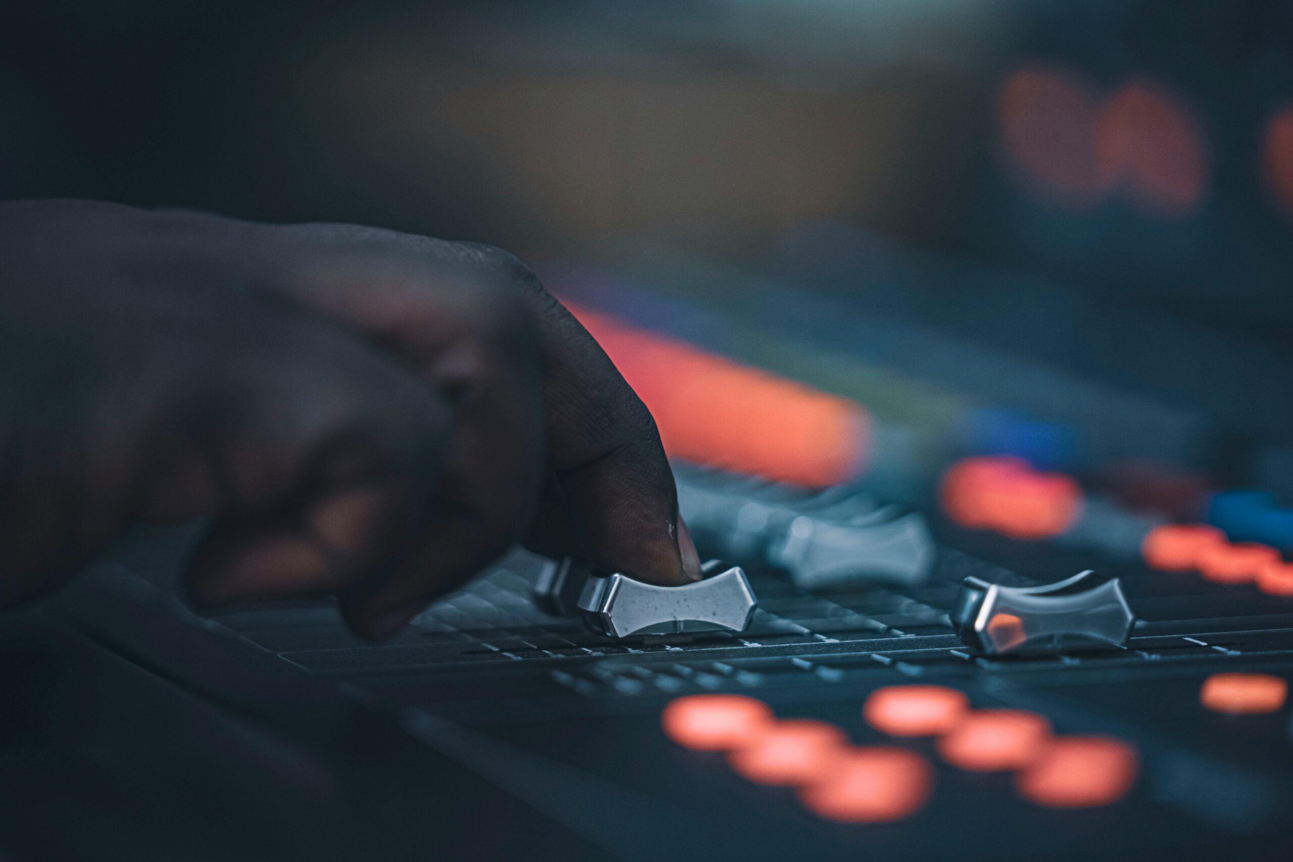 Home A hand adjusting sliders on a professional audio mixing console in a dimly lit studio setup.