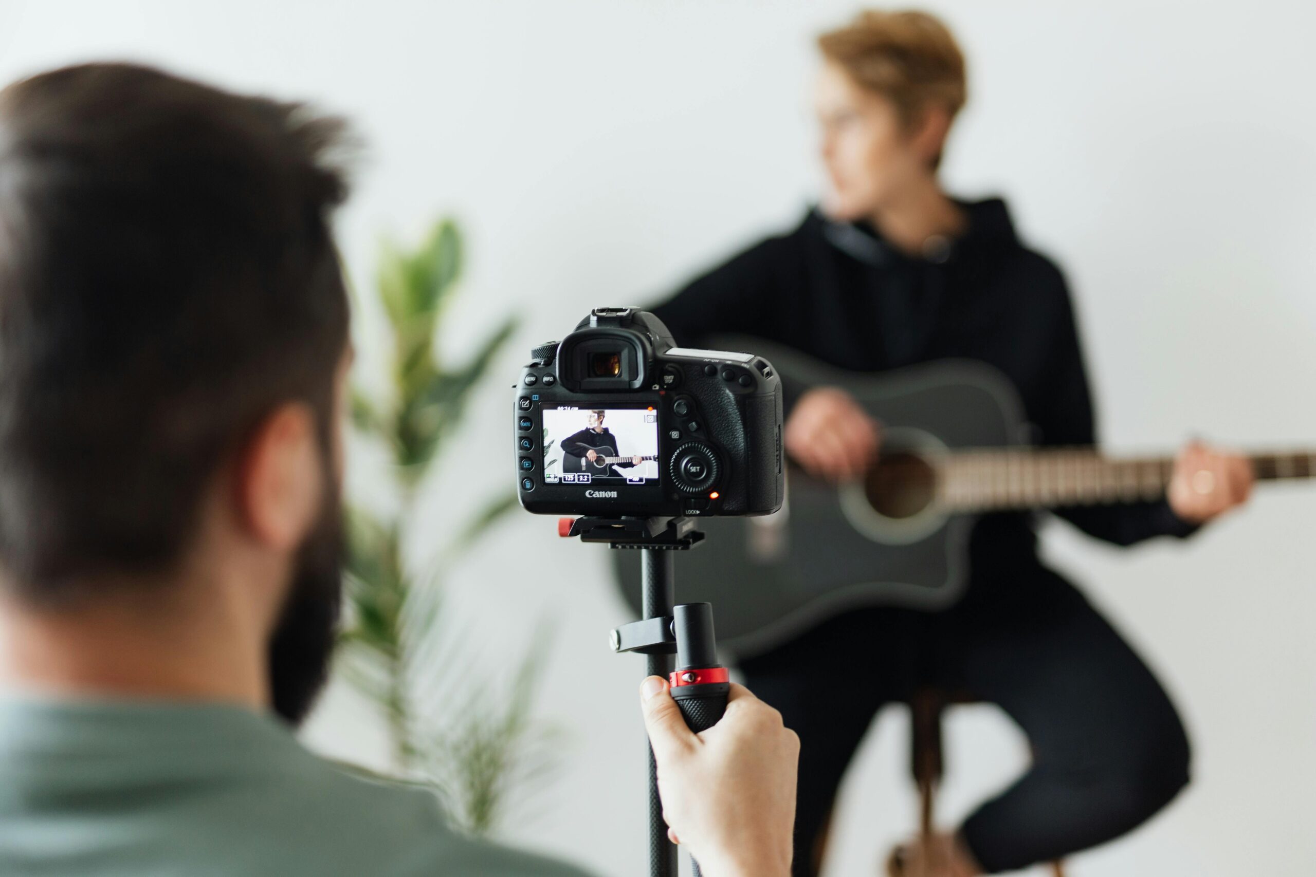 Home A photographer captures a musician playing an acoustic guitar indoors with a DSLR camera.